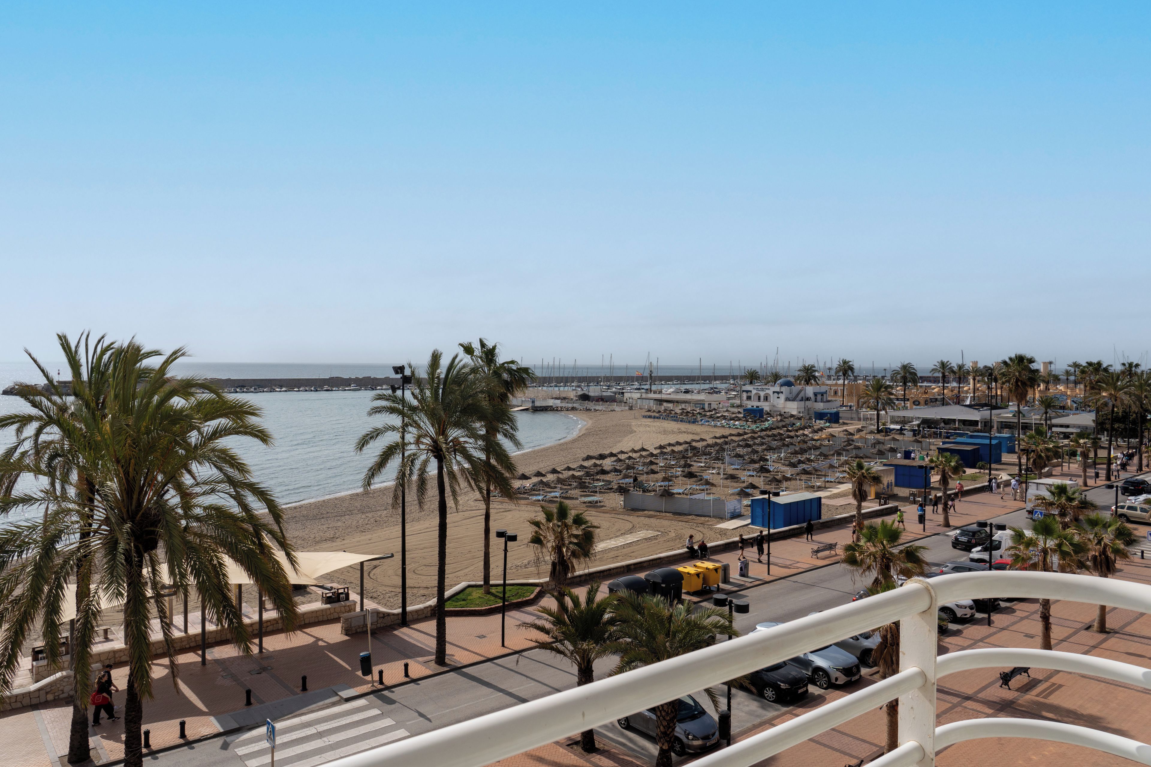 A coastal cityscape with a beach, palm trees, and a clear sky.