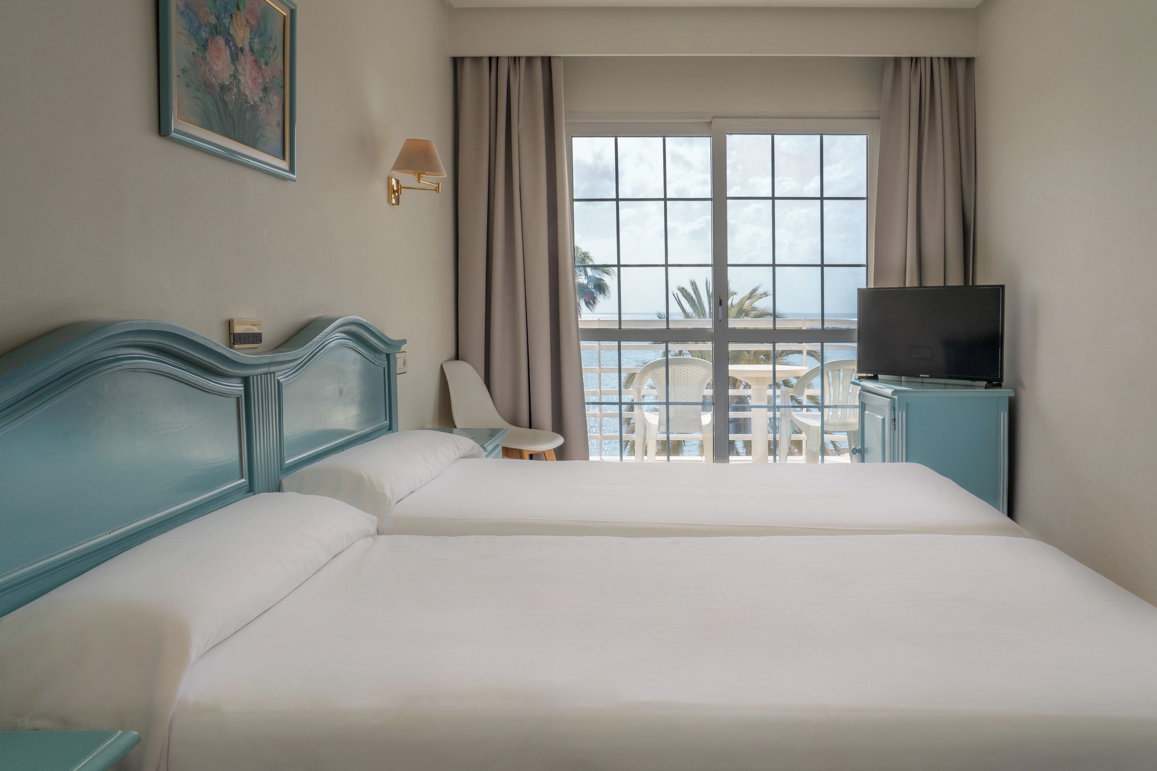 A hotel room with a bed, a TV, a chair, and a view of the sea.