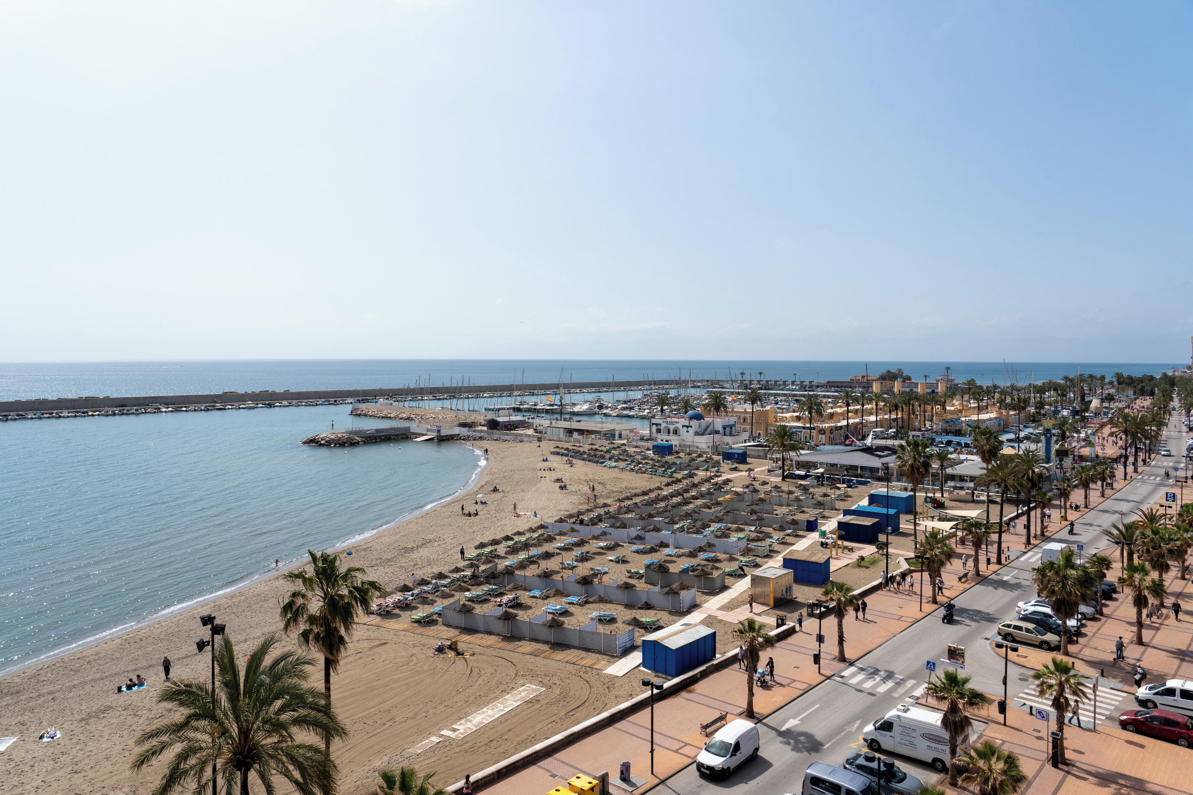 Paisaje costero con playa, puerto deportivo y calles urbanas.