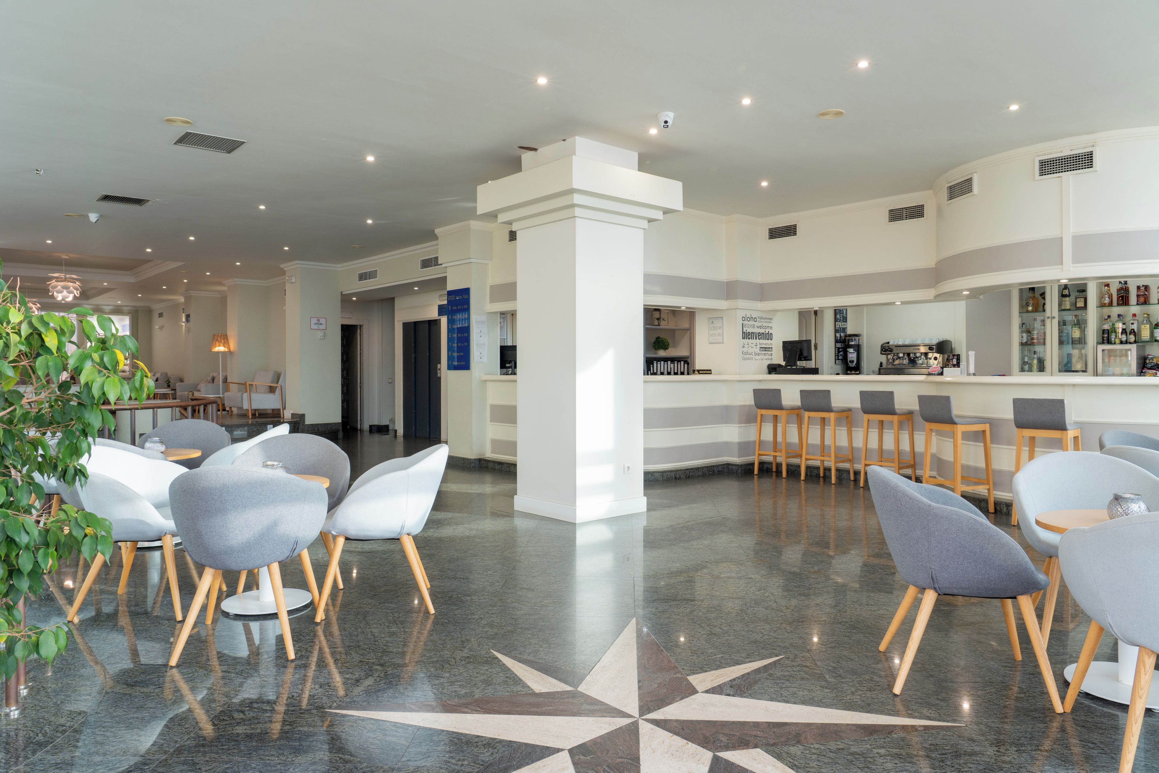 A modern hotel lobby with a bar area, seating arrangements, and a decorative floor pattern.