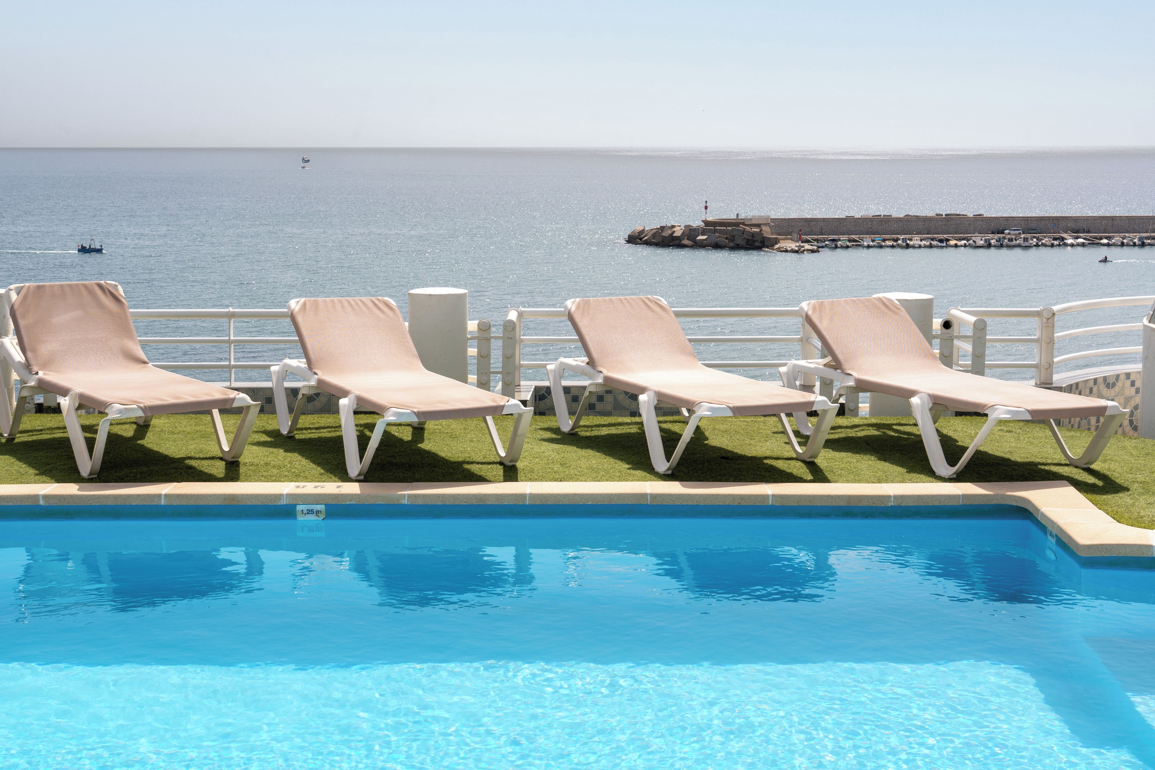 Zona de piscina con sillones de descanso y vista al mar.