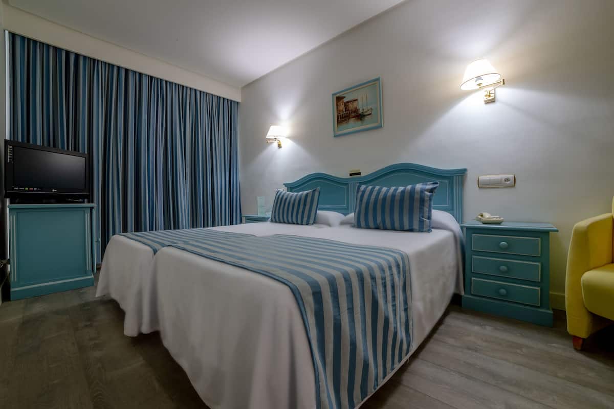 Una habitación de hotel con cama, televisión, mesita de noche y silla.