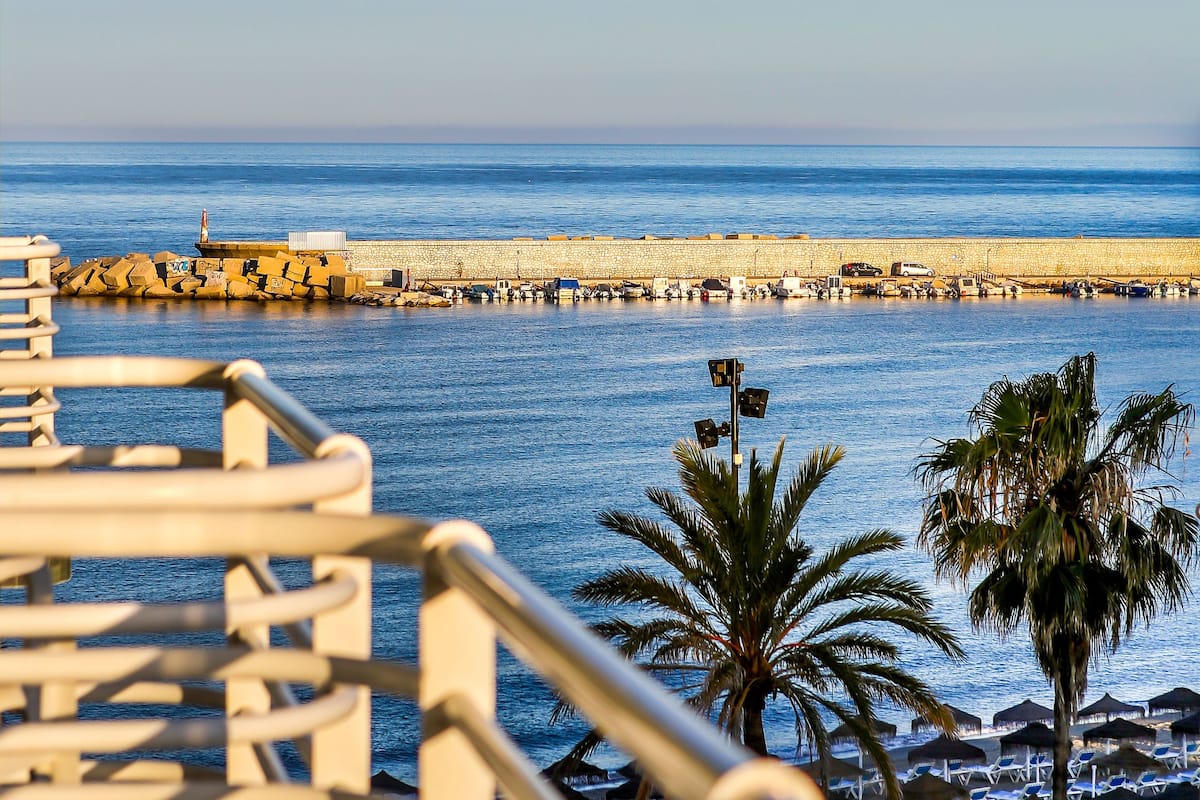 Vista de una playa con muelle, palmeras y sillas de descanso.