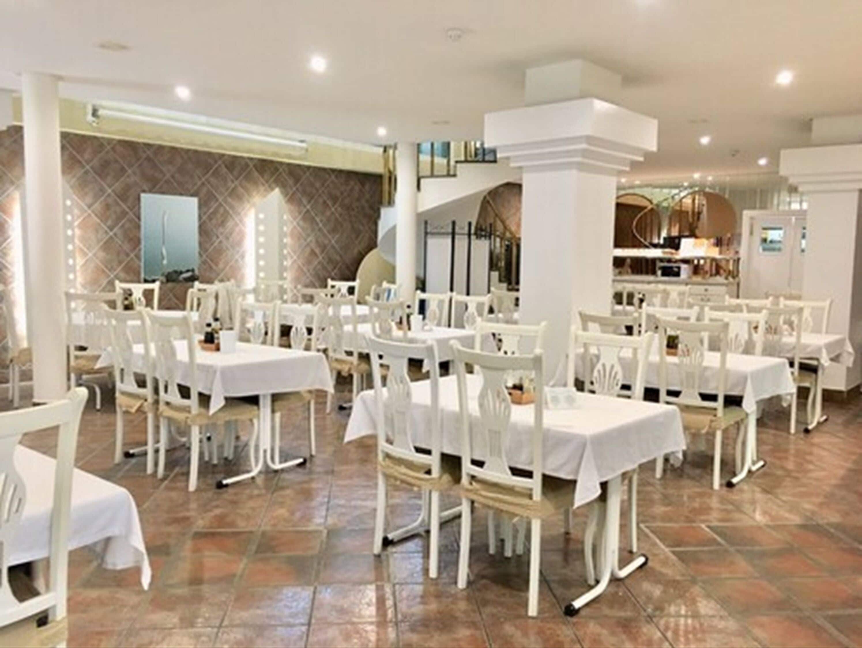 Un restaurante con mesas y sillas blancas, suelo de baldosas y un diseño de interiores moderno.