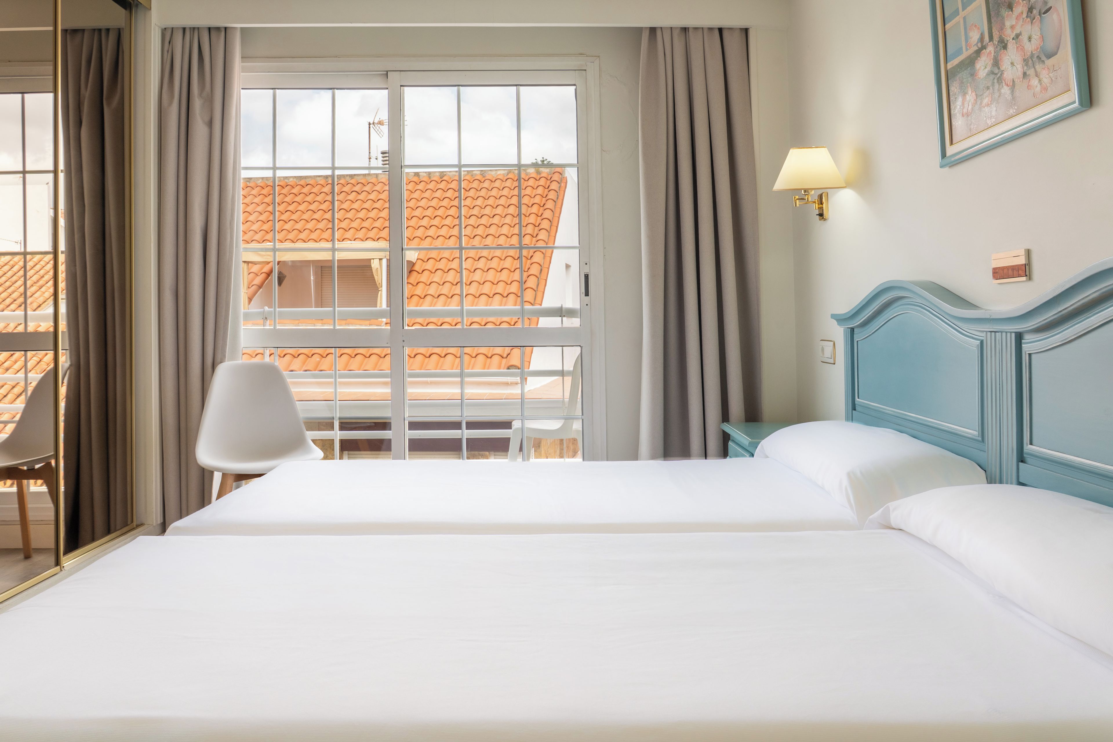 Une chambre d’hôtel avec un grand lit, une chaise, une fenêtre avec des rideaux et un tableau au mur.