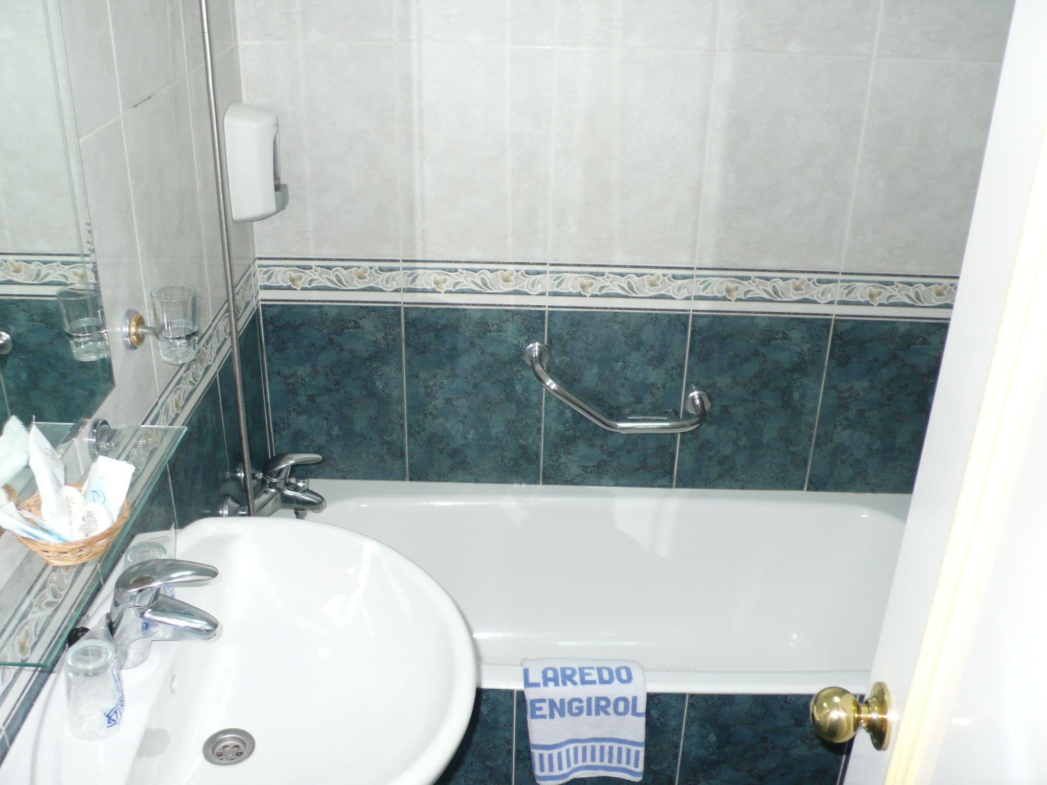 Une salle de bain avec un lavabo blanc, une baignoire et une douche. On y trouve un porte-serviettes sur lequel est accrochée une serviette.