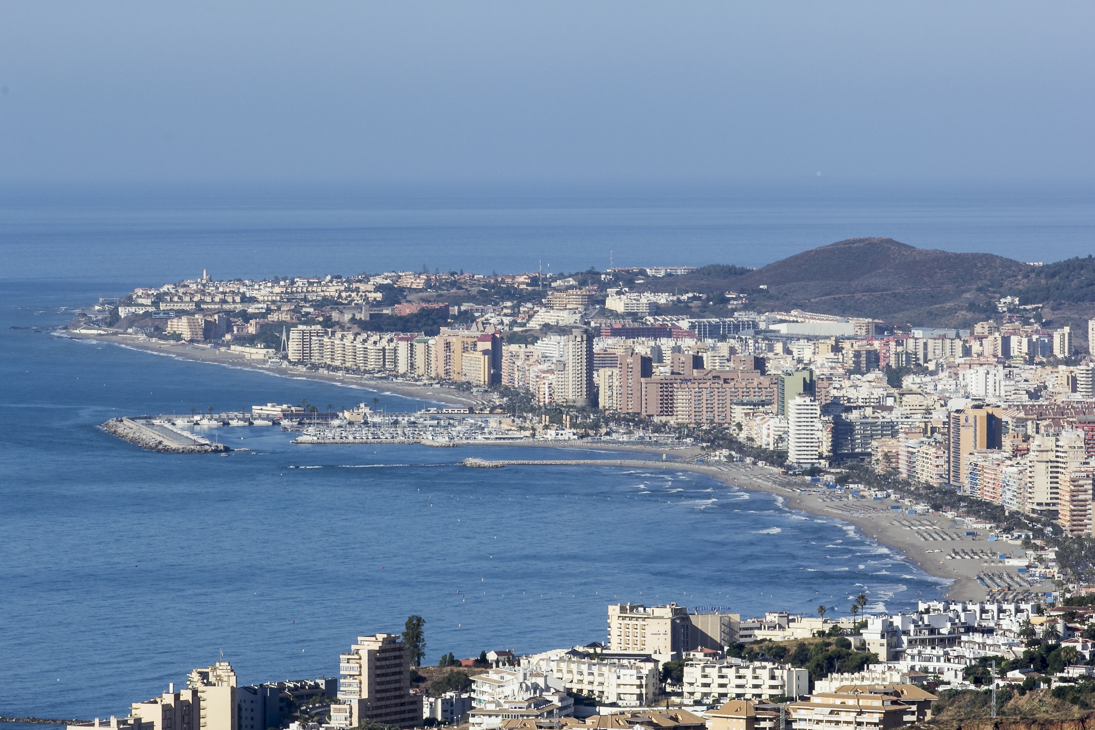 A coastal cityscape with a beach, high-rise buildings, and a hilly background.