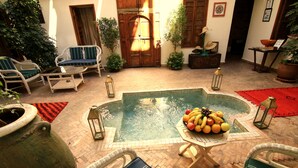 A pool area with lounge chairs, a table with fruit, and potted plants. - Riad Le Coq Berbere (Marrakech)