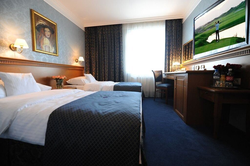 A hotel room with two beds, a desk, a chair, a television, and a painting on the wall.