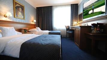 A hotel room with two beds, a desk, a chair, a television, and a painting on the wall.