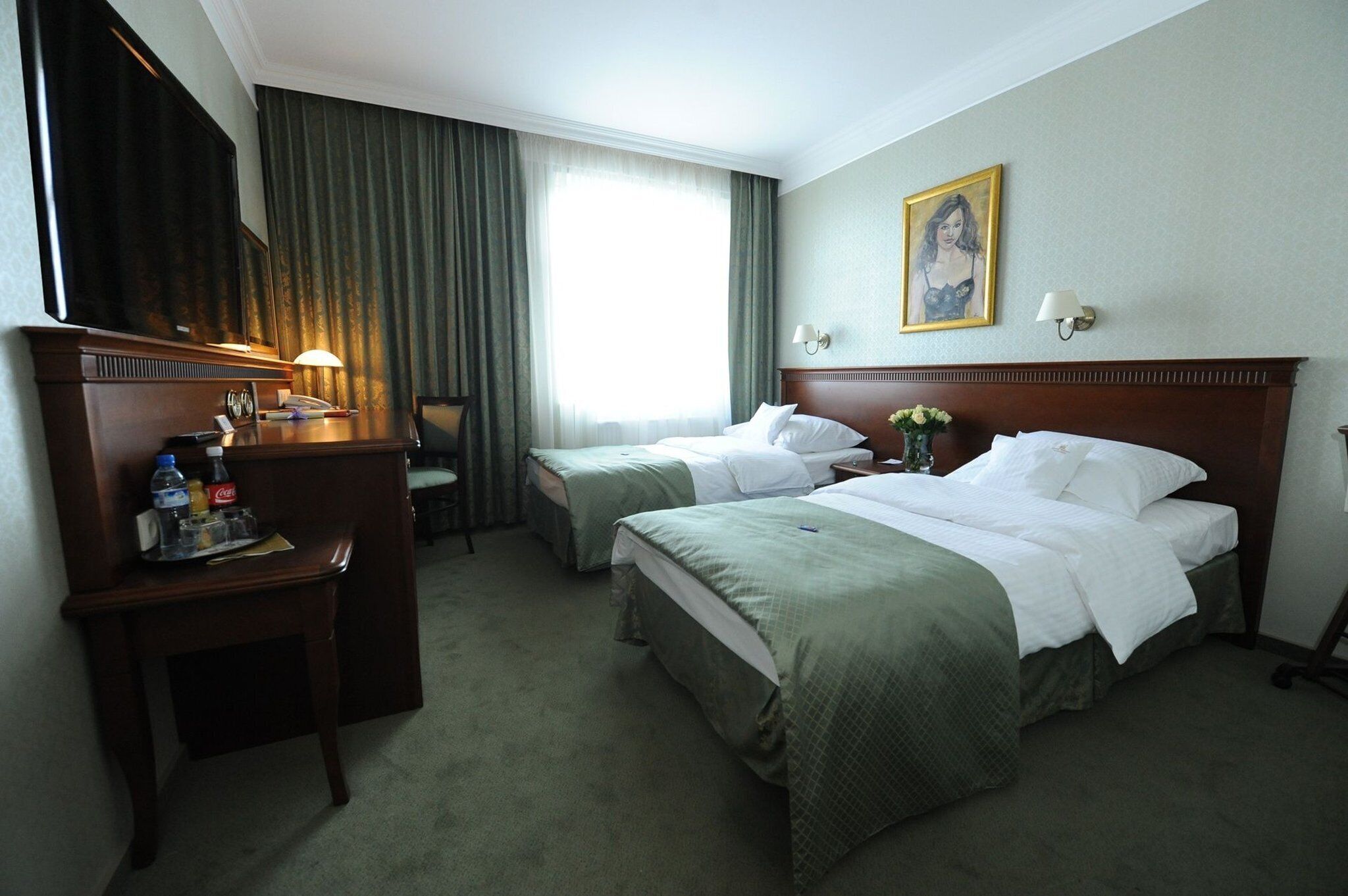 A hotel room with two beds, a desk with a chair, a television, and a window with curtains.