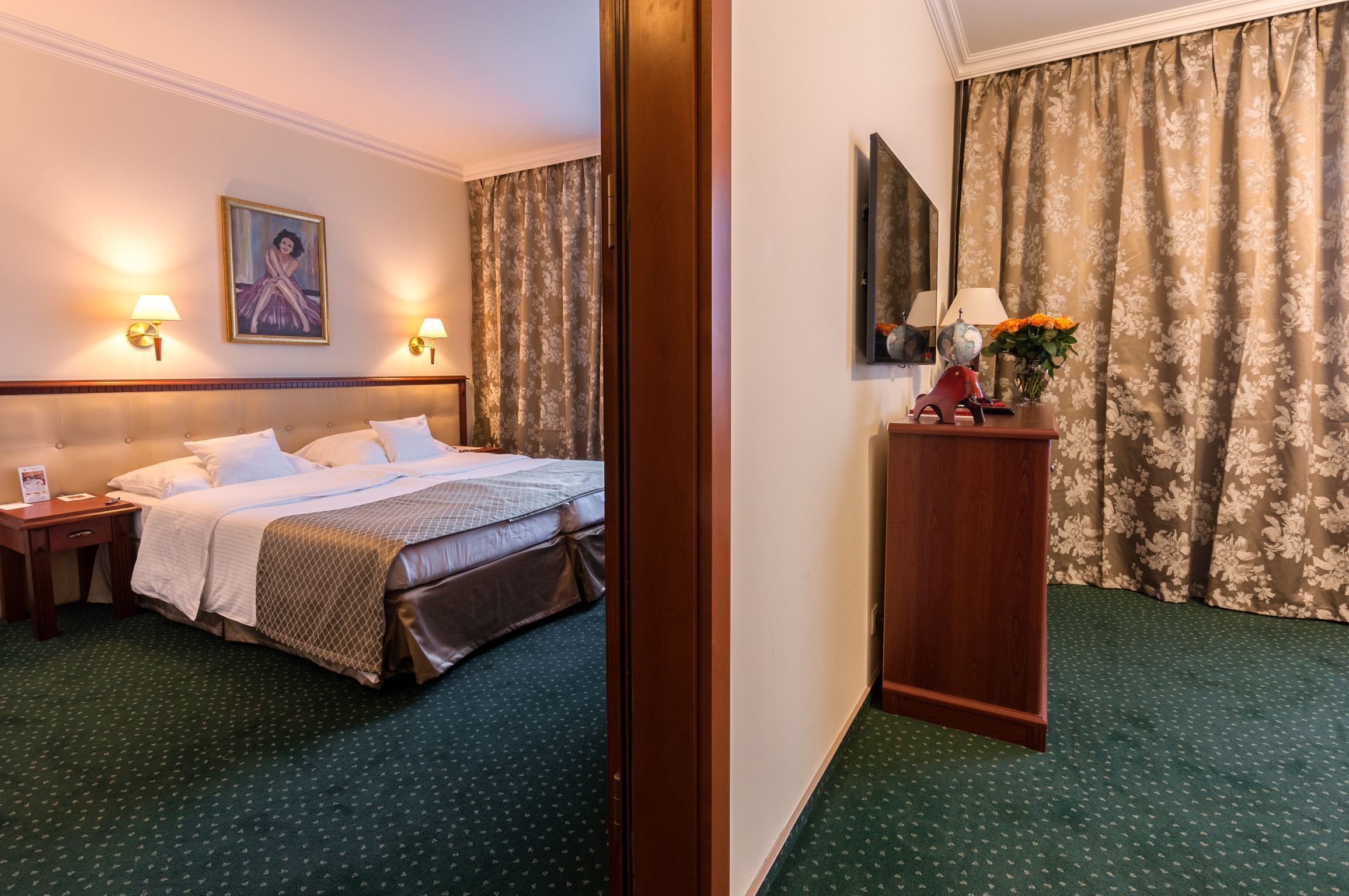 A hotel room with a bed, nightstands, a desk, a lamp, and a painting on the wall.