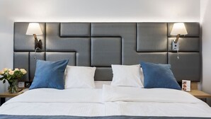 Habitación de hotel con una cama grande, dos mesitas de noche, un cabecero moderno y lámparas de pared.