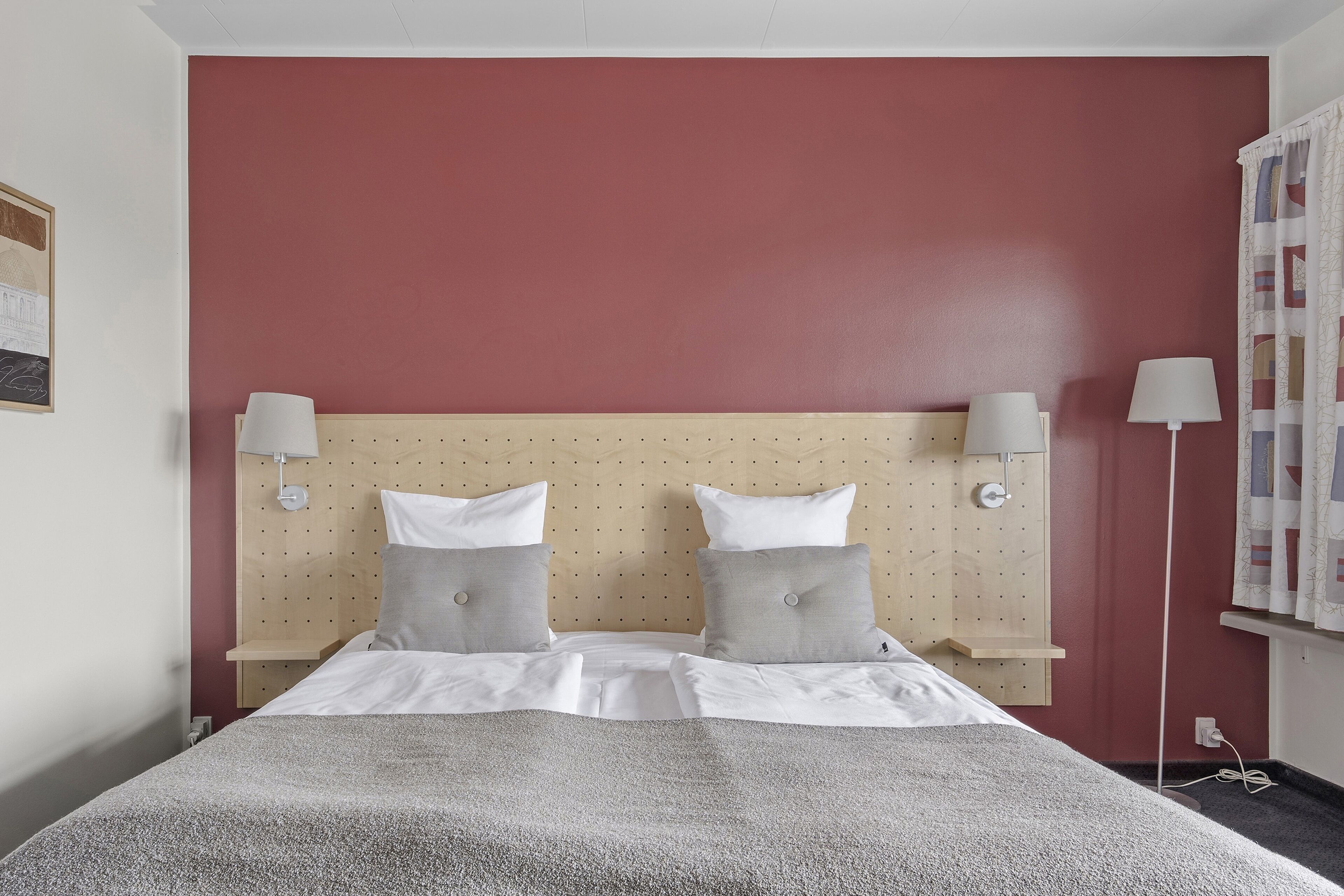 A hotel room with a bed, two bedside lamps, a headboard, and a wall-mounted shelf.
