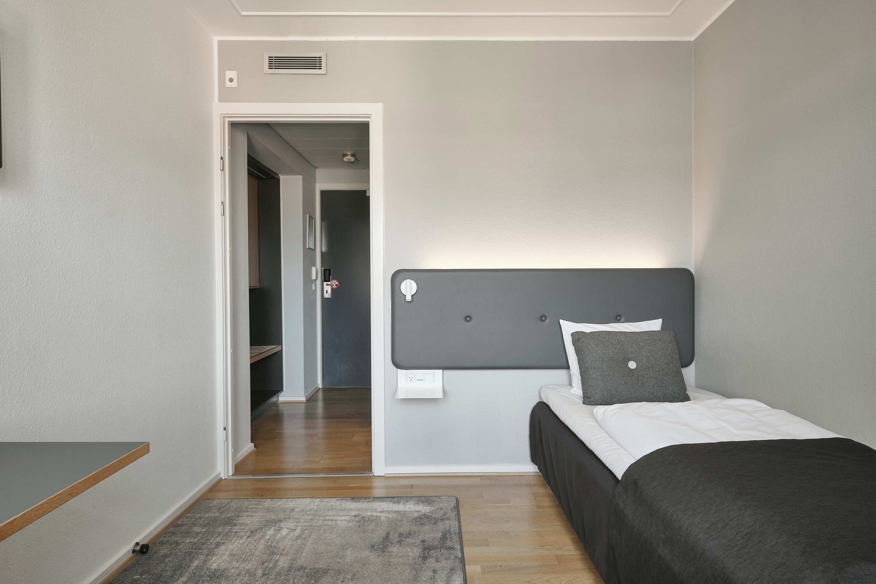 Un dormitorio con cama, mesita de noche, puerta y pasillo.