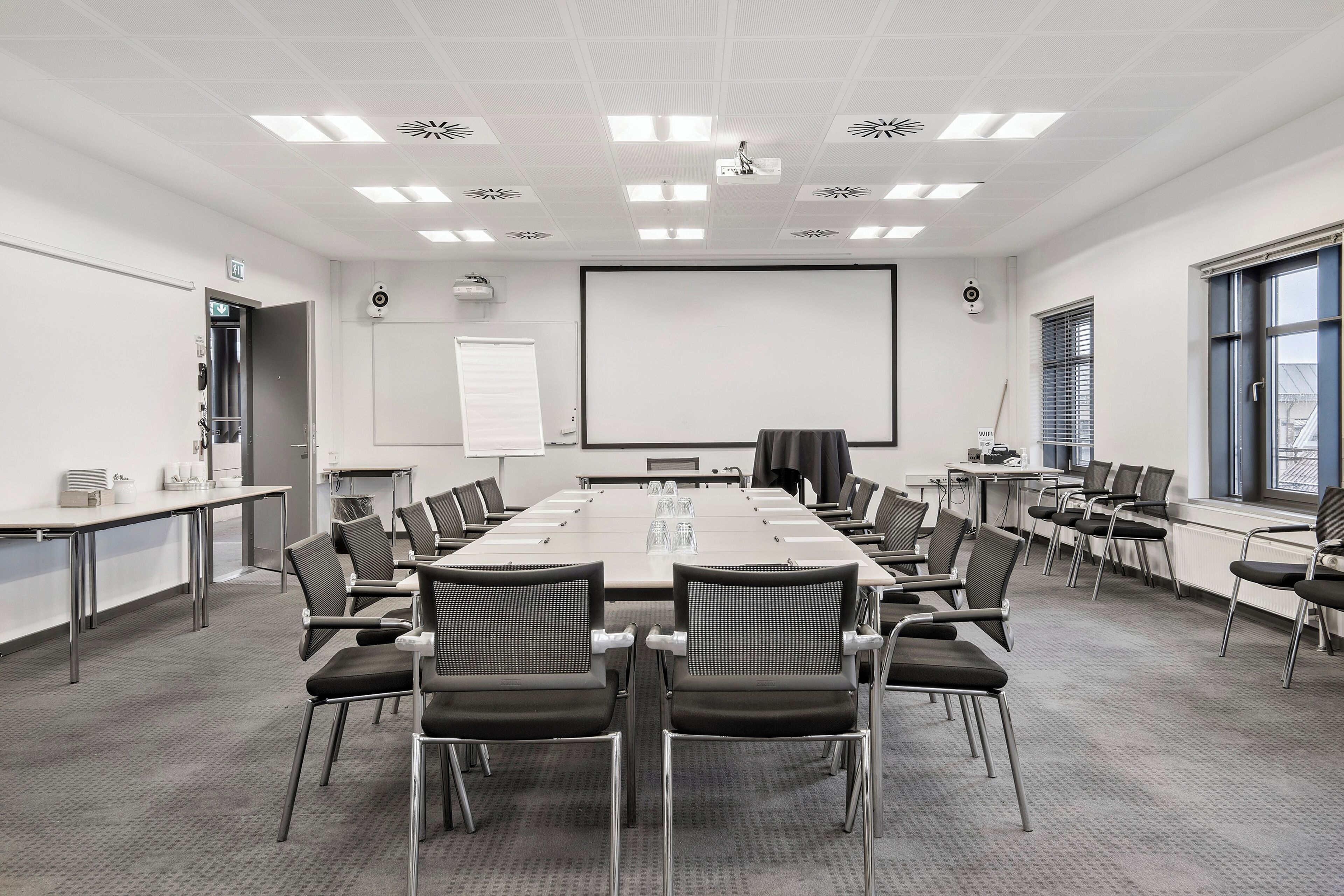A conference room with a long table, chairs, a projector screen, and a whiteboard.