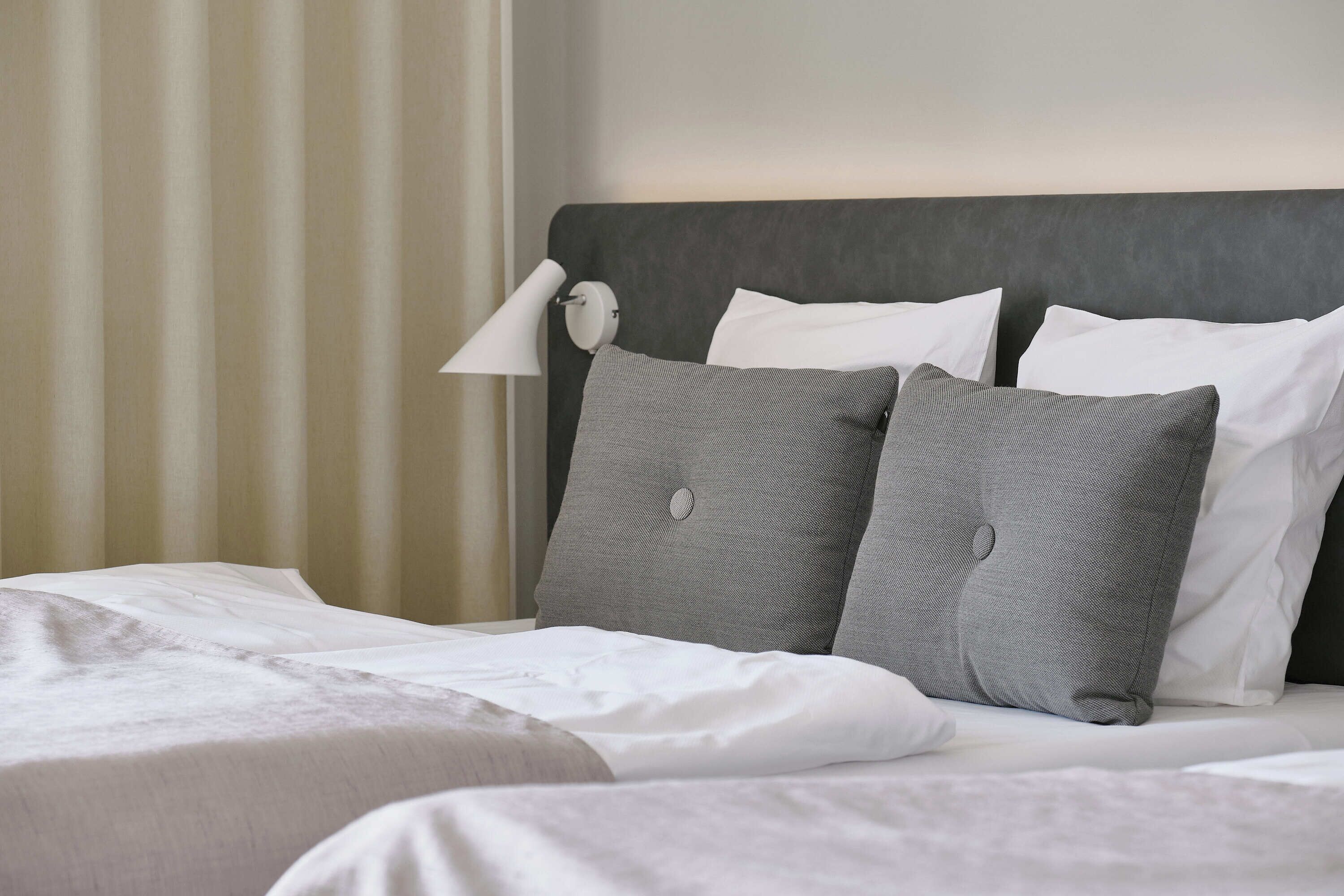 A neatly made bed with white and gray bedding, a gray headboard, and a bedside lamp.