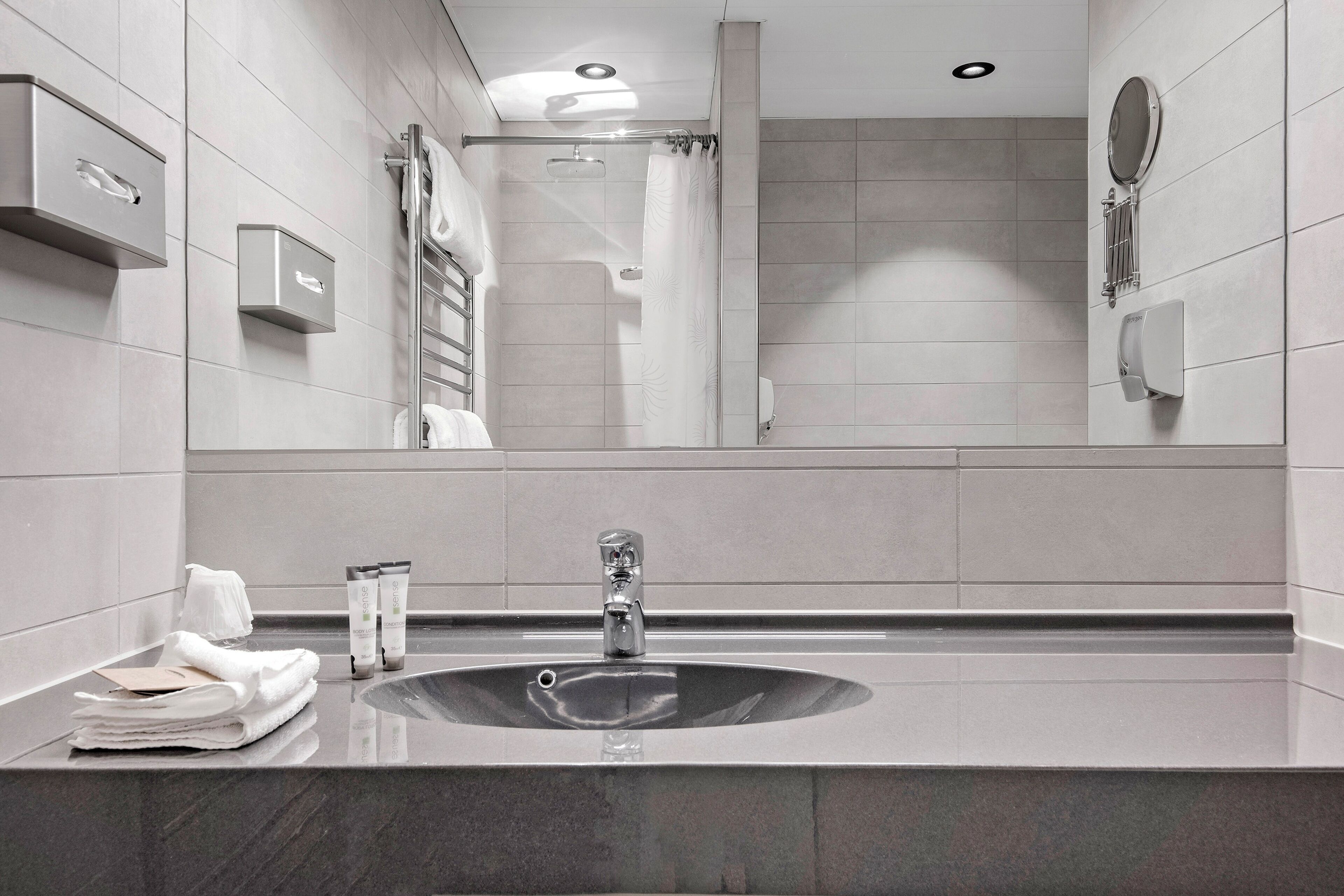 A modern bathroom with a large mirror, a sink, and a shower area.
