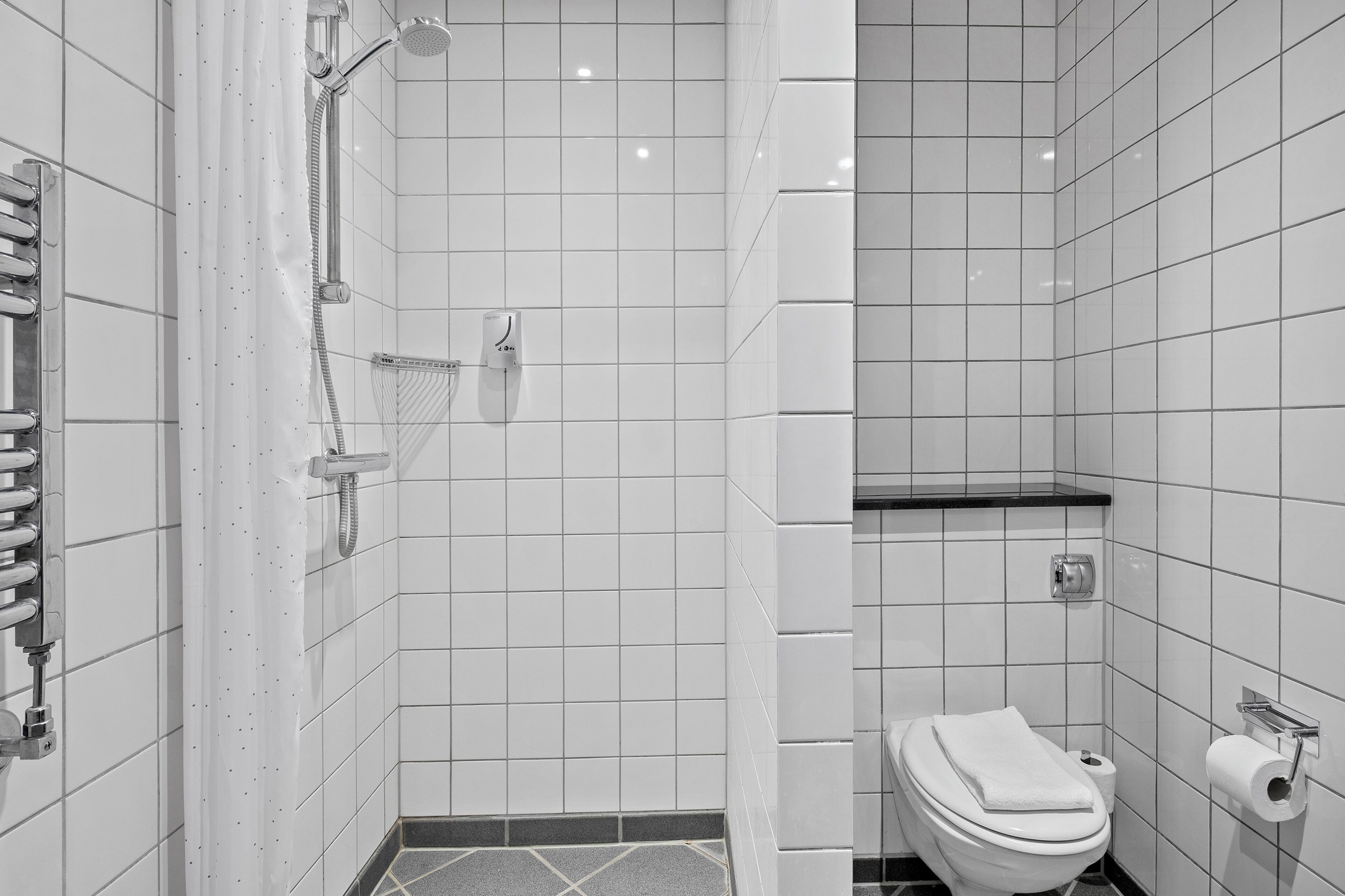 Un bagno moderno con piastrelle bianche, una doccia, un water e un porta asciugamani.