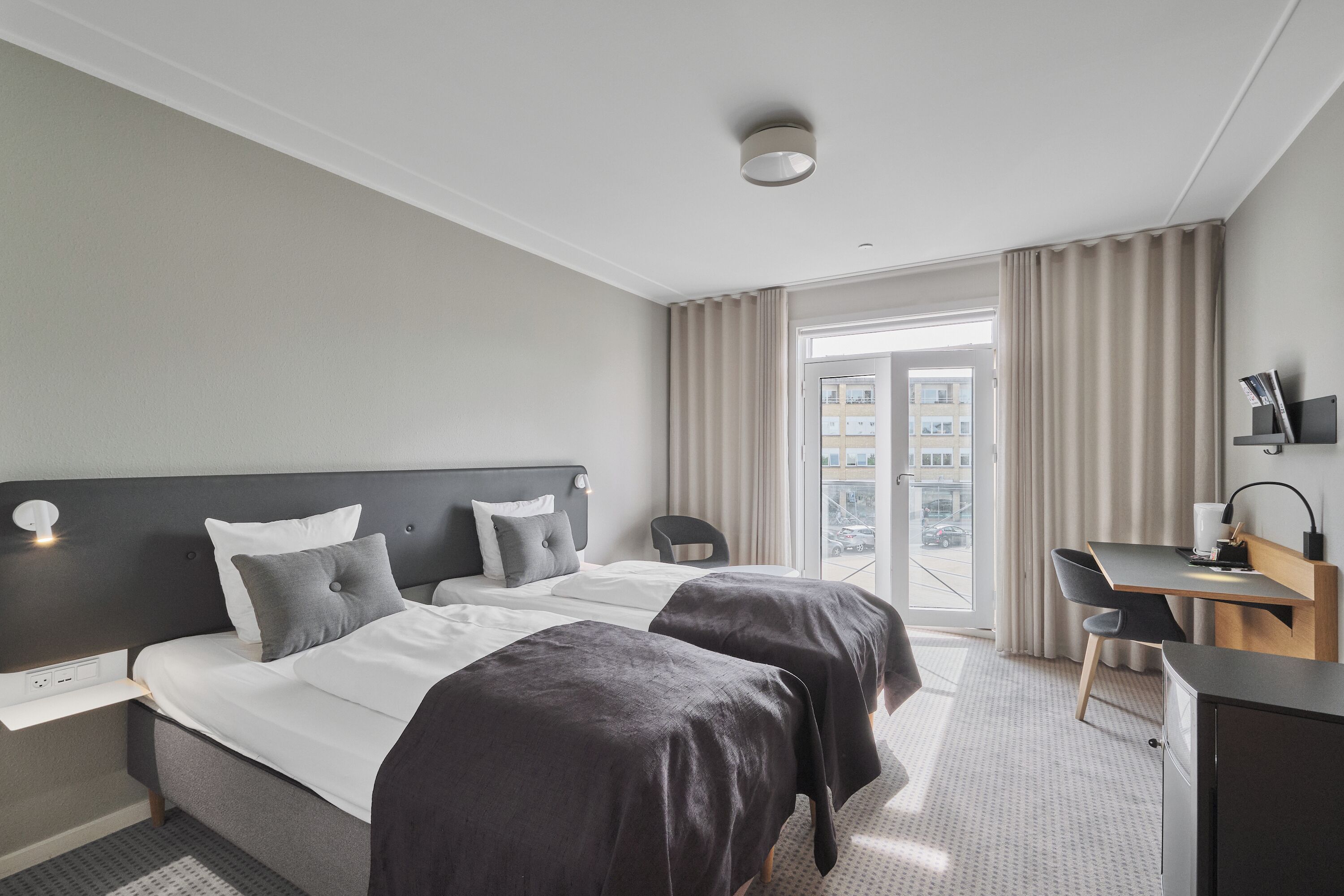 A hotel room with two beds, a desk, a chair, and a TV.