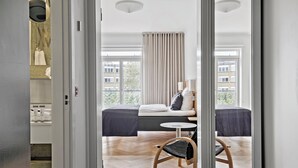 A hotel room with a bed, two bedside tables, a chair, and a view of the city through large windows. - Hotel Svendborg (Svendborg)