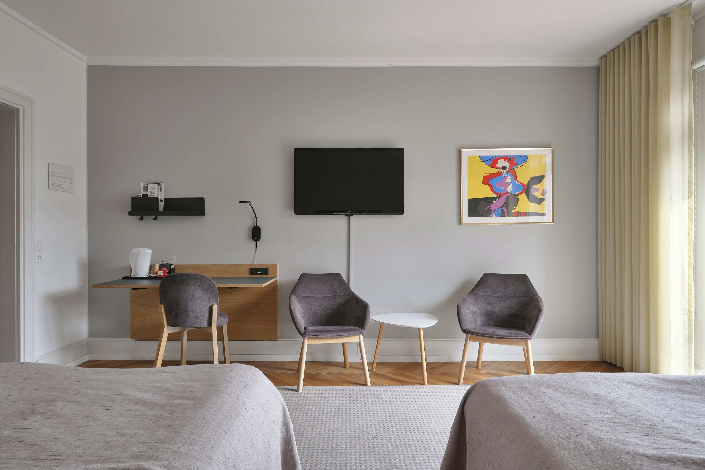 Una habitació d'hotel amb dos llits, un escriptori amb televisió de pantalla plana, dues cadires, una taula petita i un quadre a la paret.