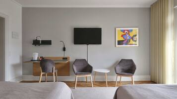 Una habitació d'hotel amb dos llits, un escriptori amb televisió de pantalla plana, dues cadires, una taula petita i un quadre a la paret.