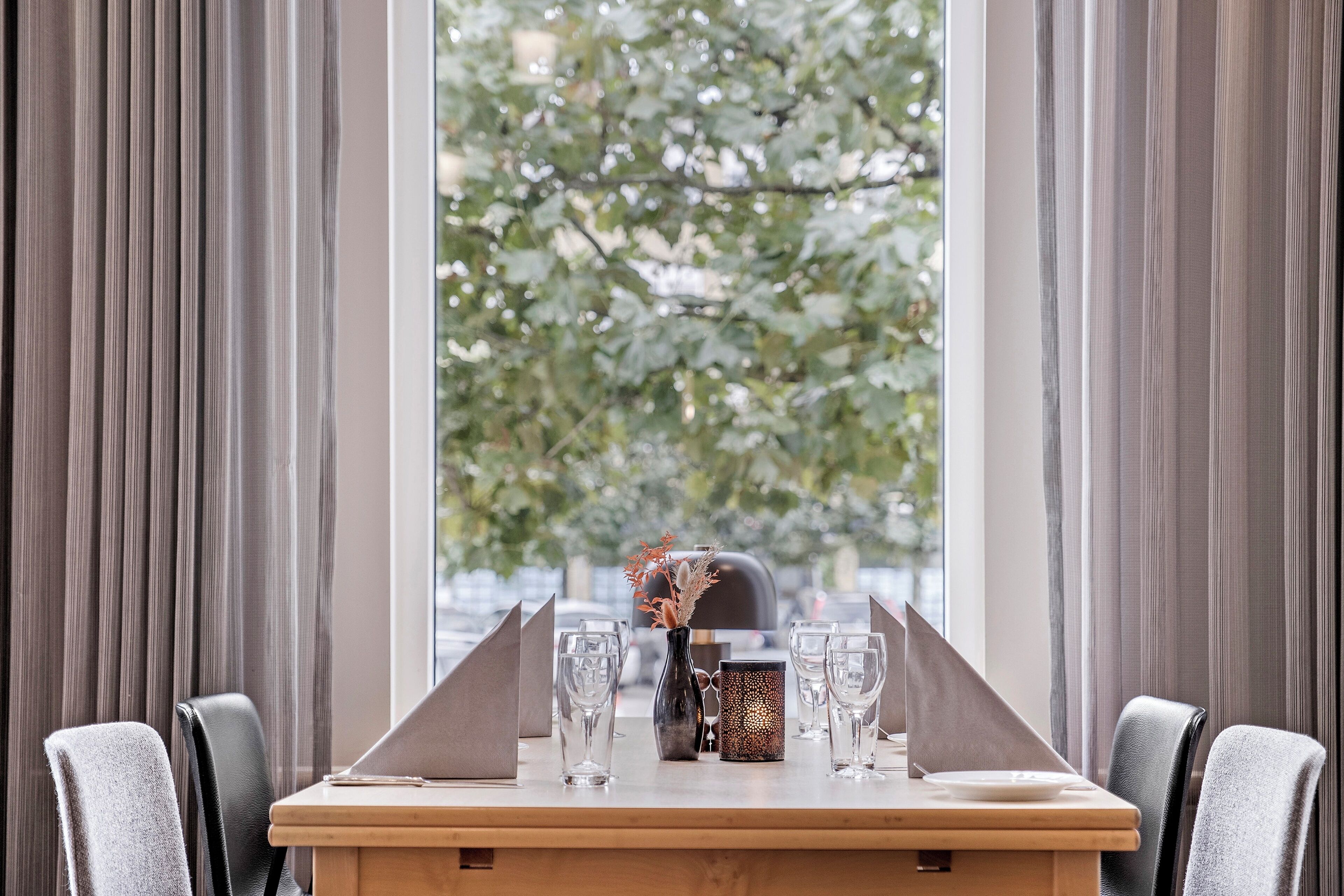 A dining table set for two with a vase of dried flowers, two glasses, and a menu stand.