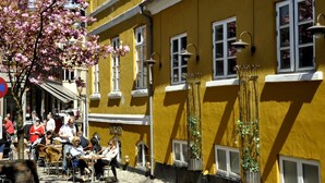 A yellow building with white window frames and a red roof. There are outdoor tables and chairs where people are sitting and eating. - Hotel Svendborg (Svendborg)