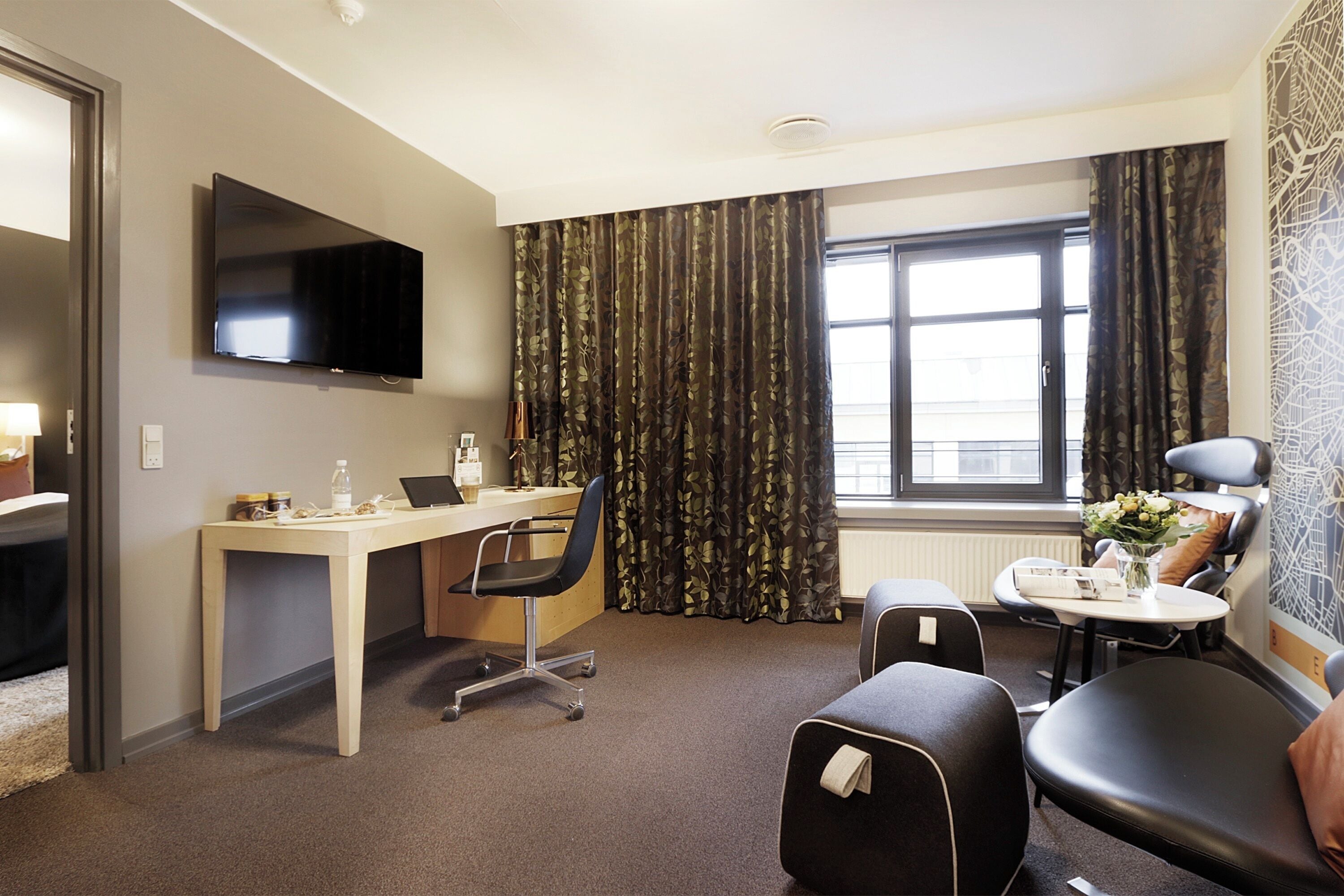 A hotel room with a desk, chair, and a television on the wall.