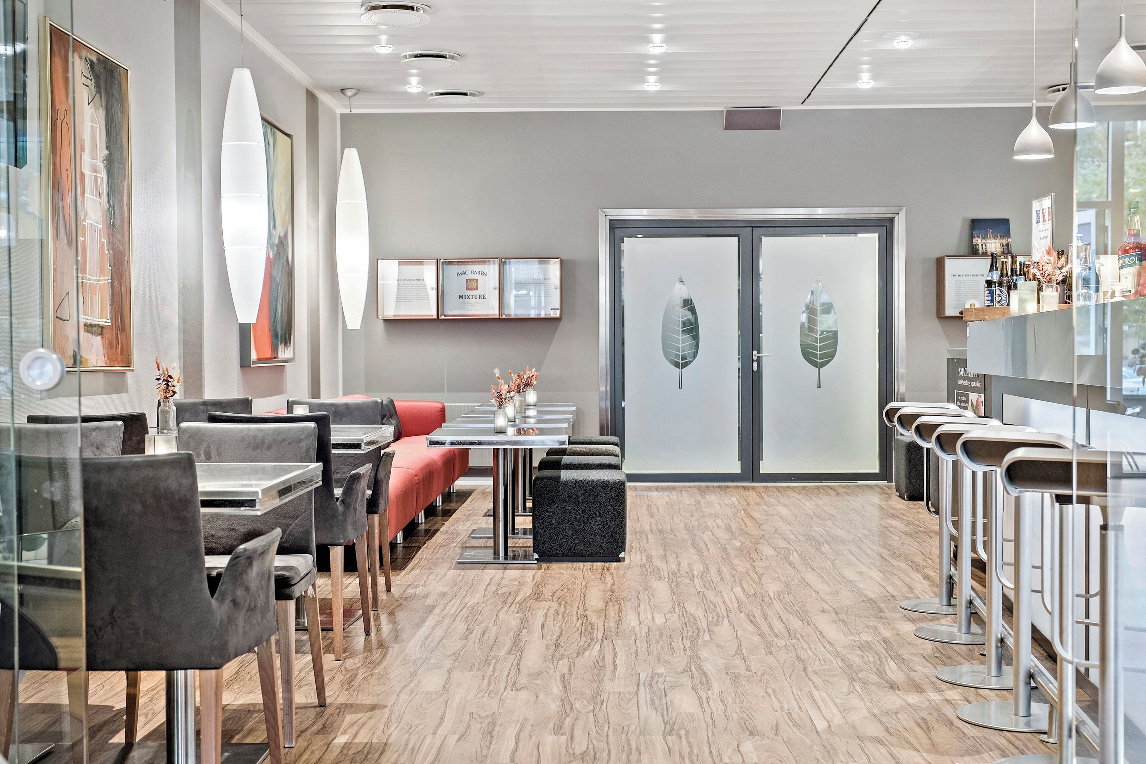 A modern restaurant with a wooden floor, grey and red seating, and framed artwork on the walls.