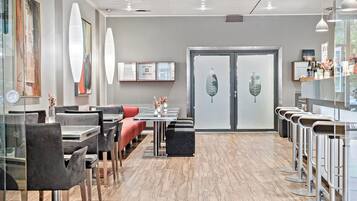 A modern restaurant with a wooden floor, grey and red seating, and framed artwork on the walls.