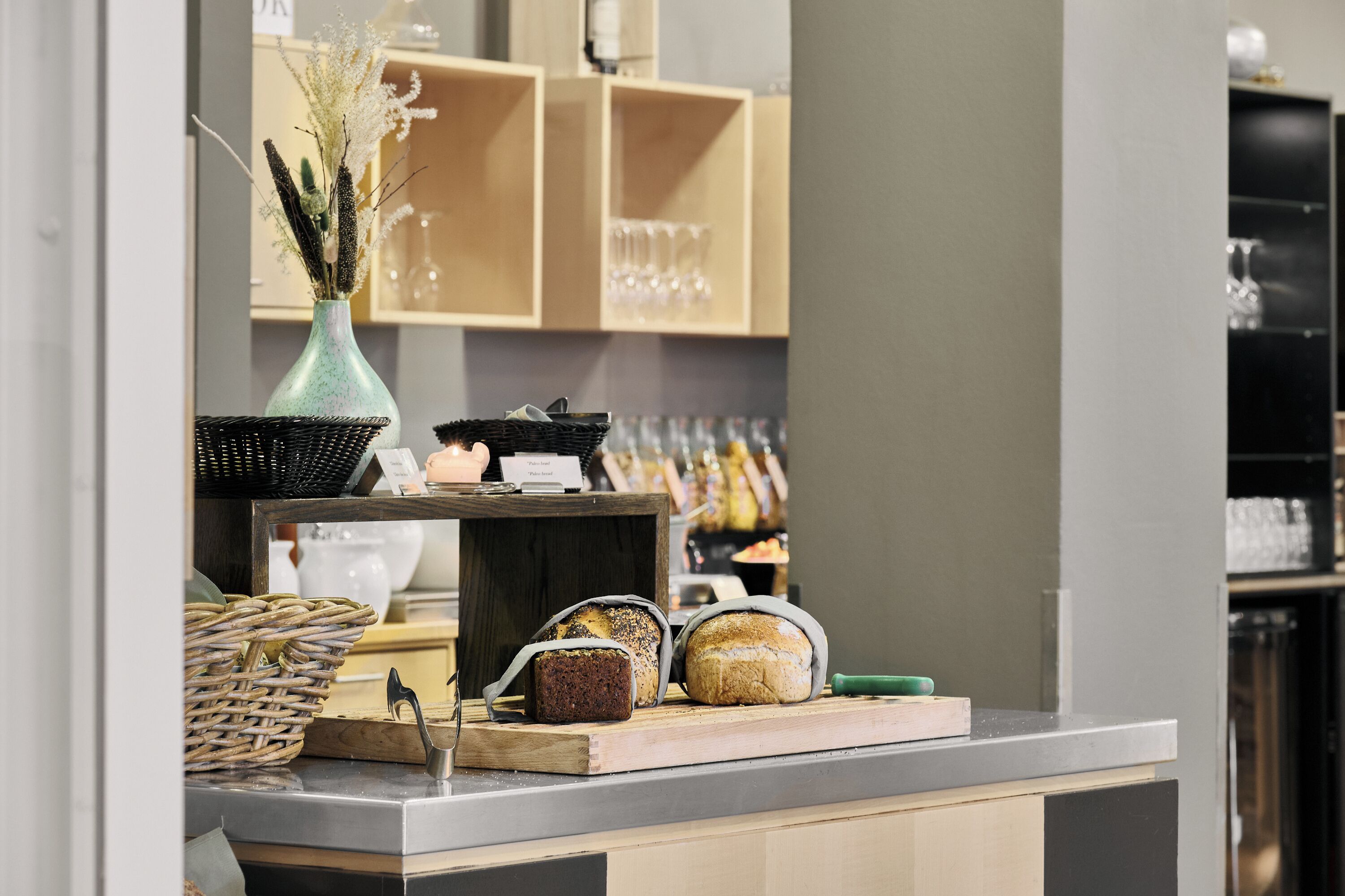 A bakery display with various breads and a vase of dried flowers.