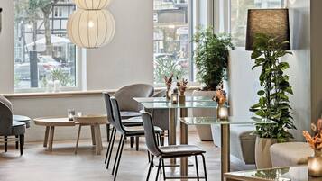 Un interior moderno con una mesa de comedor de vidrio, varias sillas, una planta alta en maceta y un ventanal con vistas a la calle.