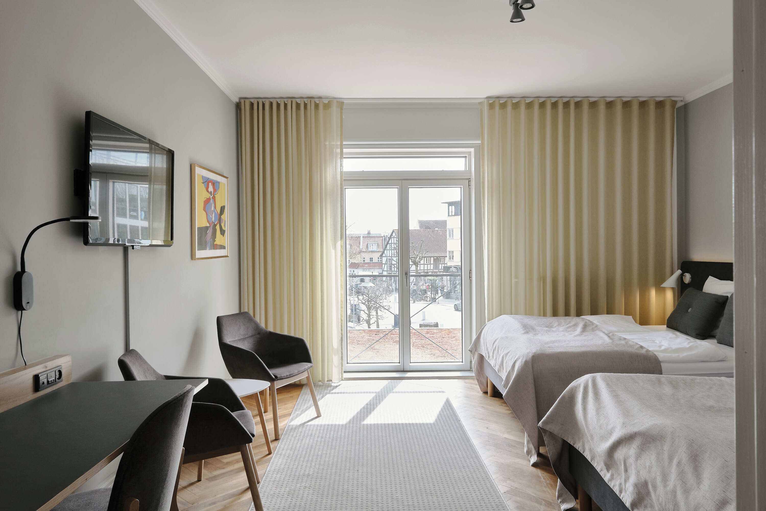 A hotel room with a bed, a desk, a chair, a TV, and a window with curtains.