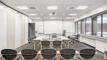Une salle de conférence avec une longue table, des chaises, un projecteur et de grandes fenêtres.