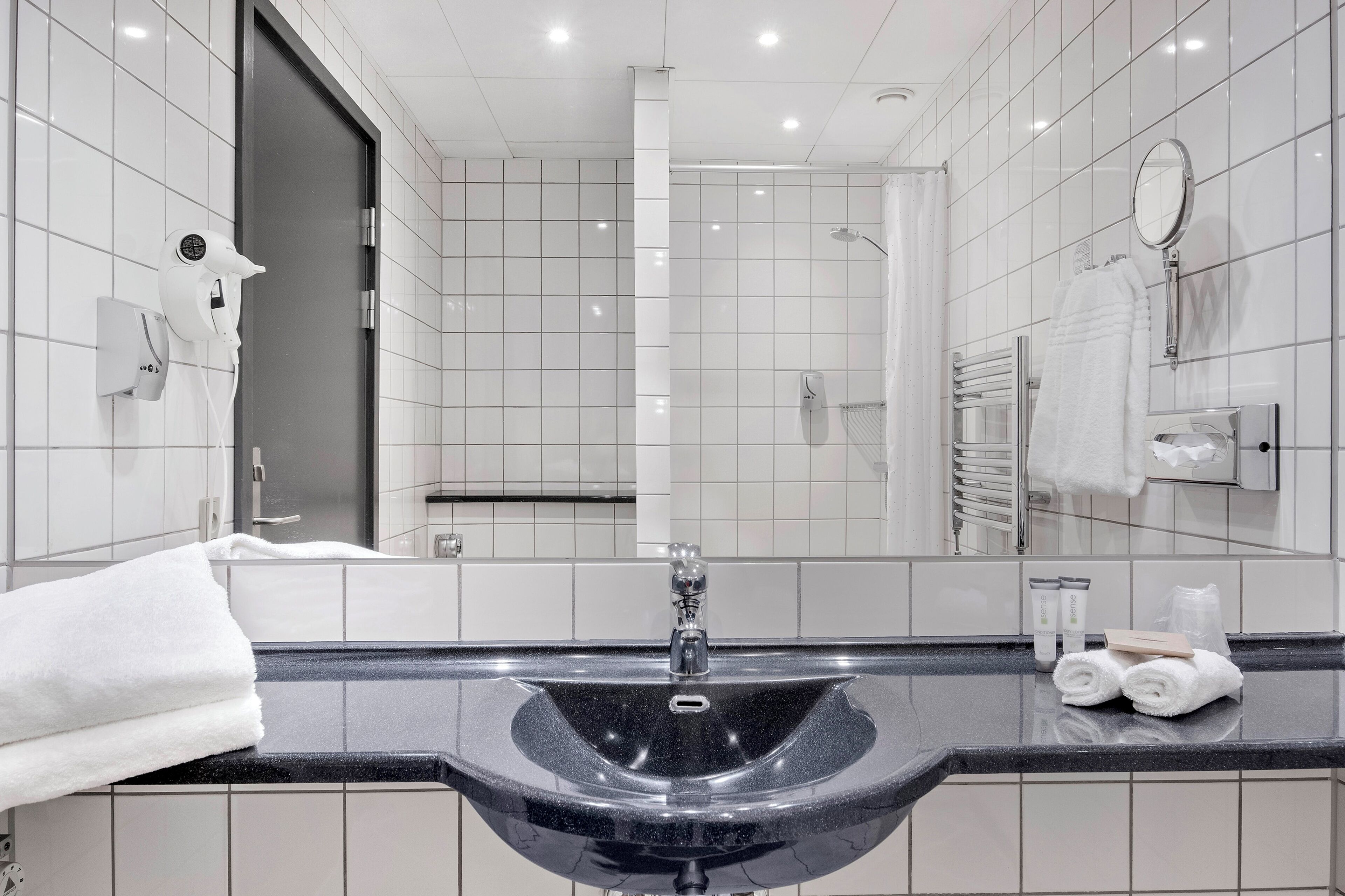 Une salle de bain moderne avec un lavabo noir, des carreaux blancs, un porte-serviettes et un miroir.