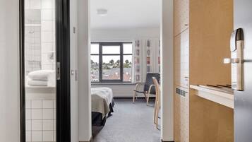 Habitación de hotel con cama, una silla, un armario de madera y vistas al exterior.