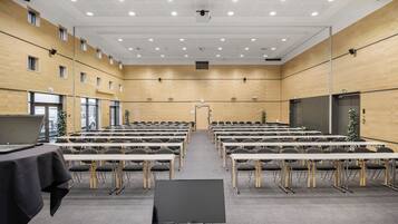 Un salón de conferencias con filas de mesas y sillas, una pantalla grande al frente y una puerta en la parte posterior.