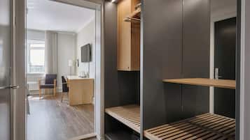 Una habitación de hotel moderna con un escritorio de madera, una silla, un televisor y un vestidor con estantes y espacio para colgar.