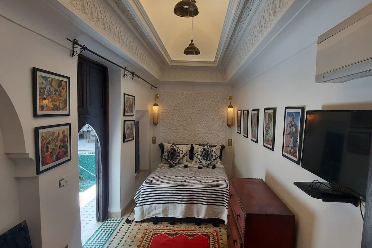 Un corridoio stretto conduce a una camera da letto con un letto, una cassettiera e un televisore.