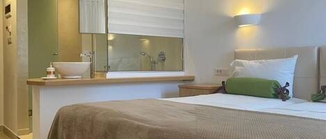 Habitación de hotel con cama, mesita de noche, baño con lavamanos y espejo.