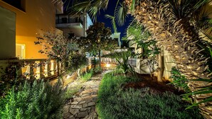 A stone pathway flanked by lush greenery and palm trees, leading to a building with a balcony. - Malia Mare (Hersonissos)