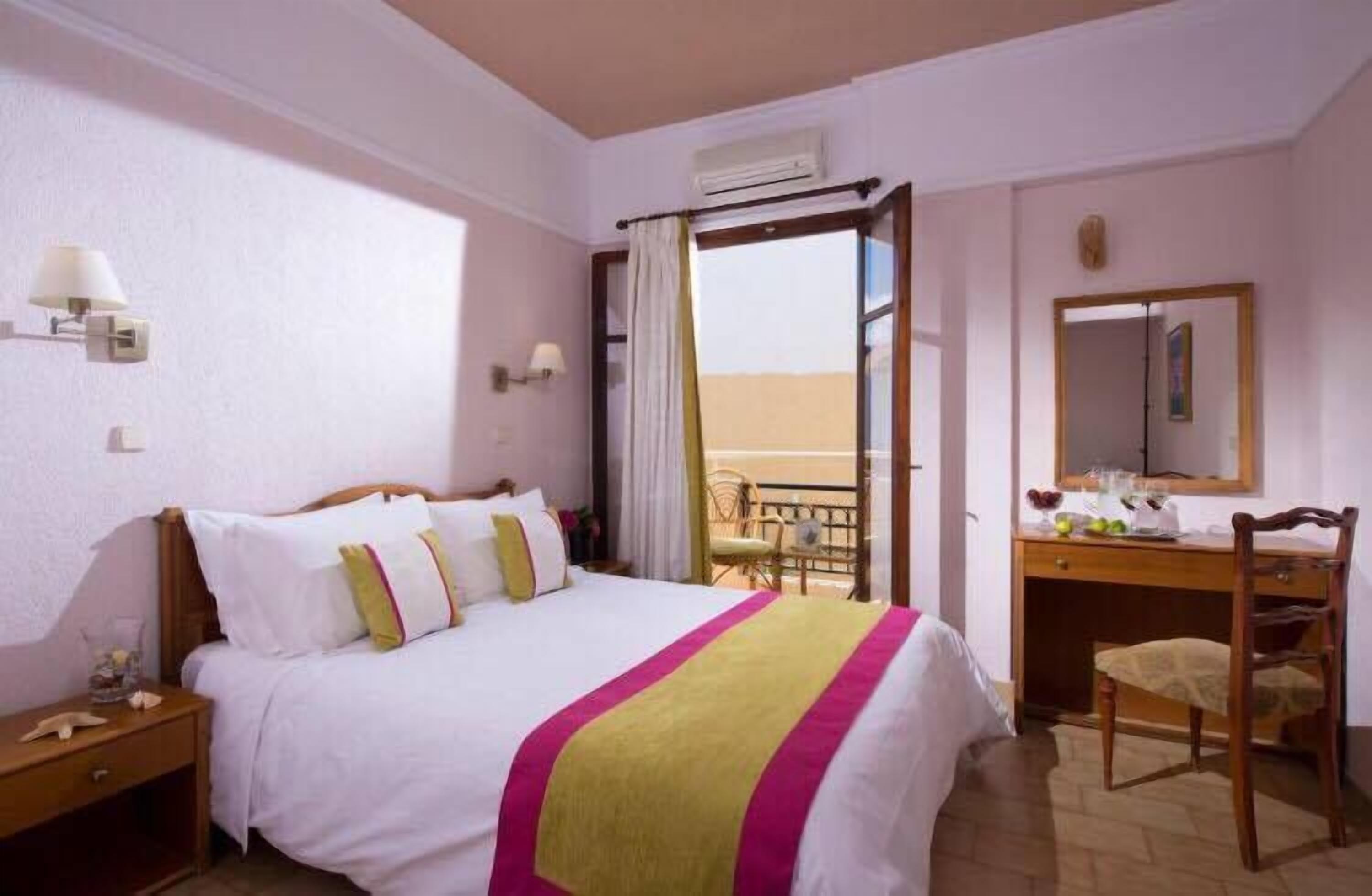 Habitación de hotel con cama, escritorio, silla, ventana con vistas y espejo.
