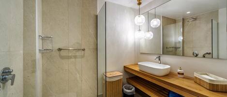 Un baño moderno con ducha de vidrio, un espejo grande y un tocador de madera con dos lavamanos.