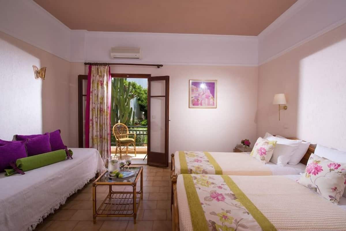 A hotel room with two beds, a small table, a chair, a balcony with a view, and a framed picture on the wall.