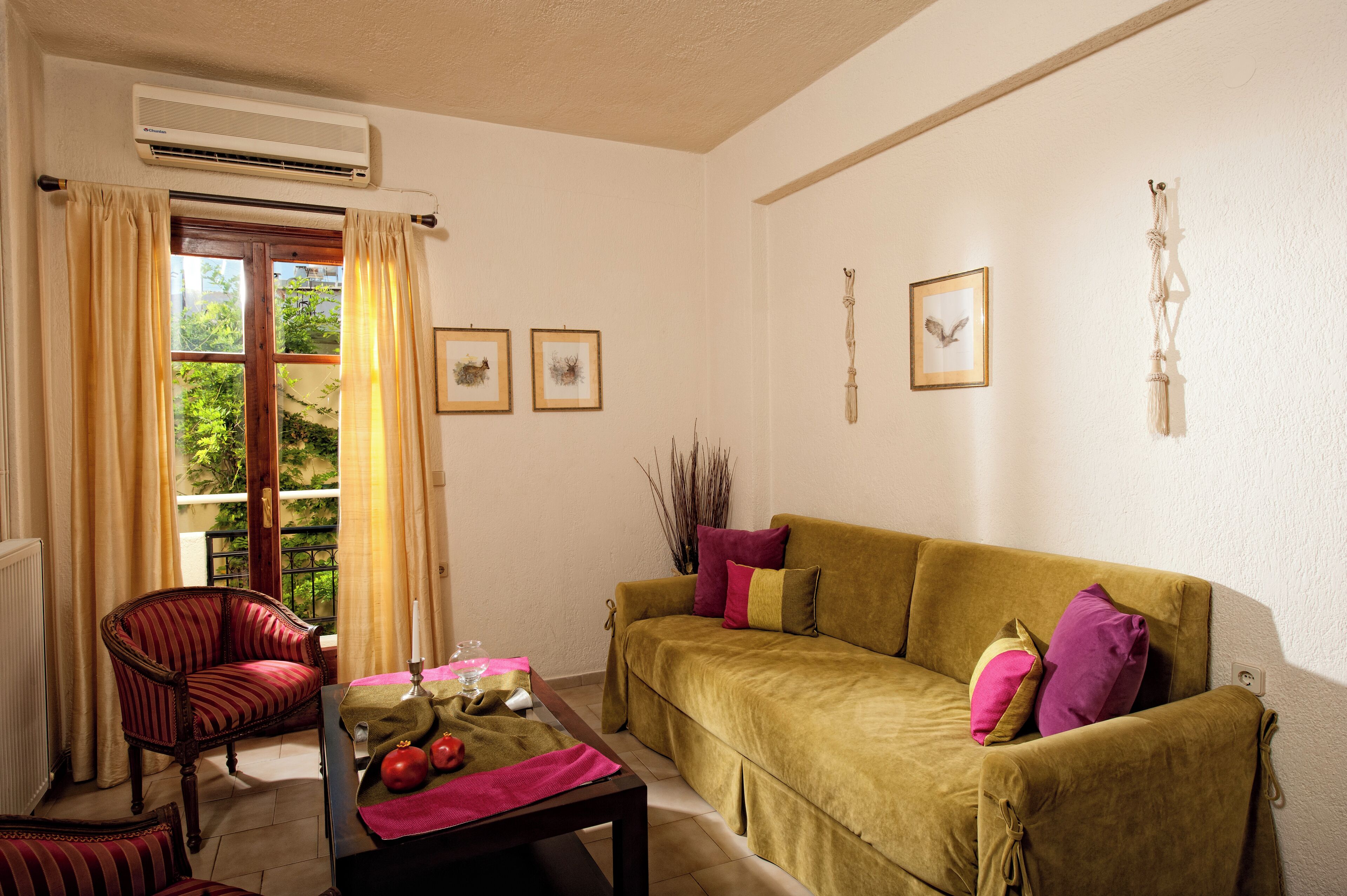 A living room with a sofa, a chair, a table with a vase and fruit, and a window with curtains.