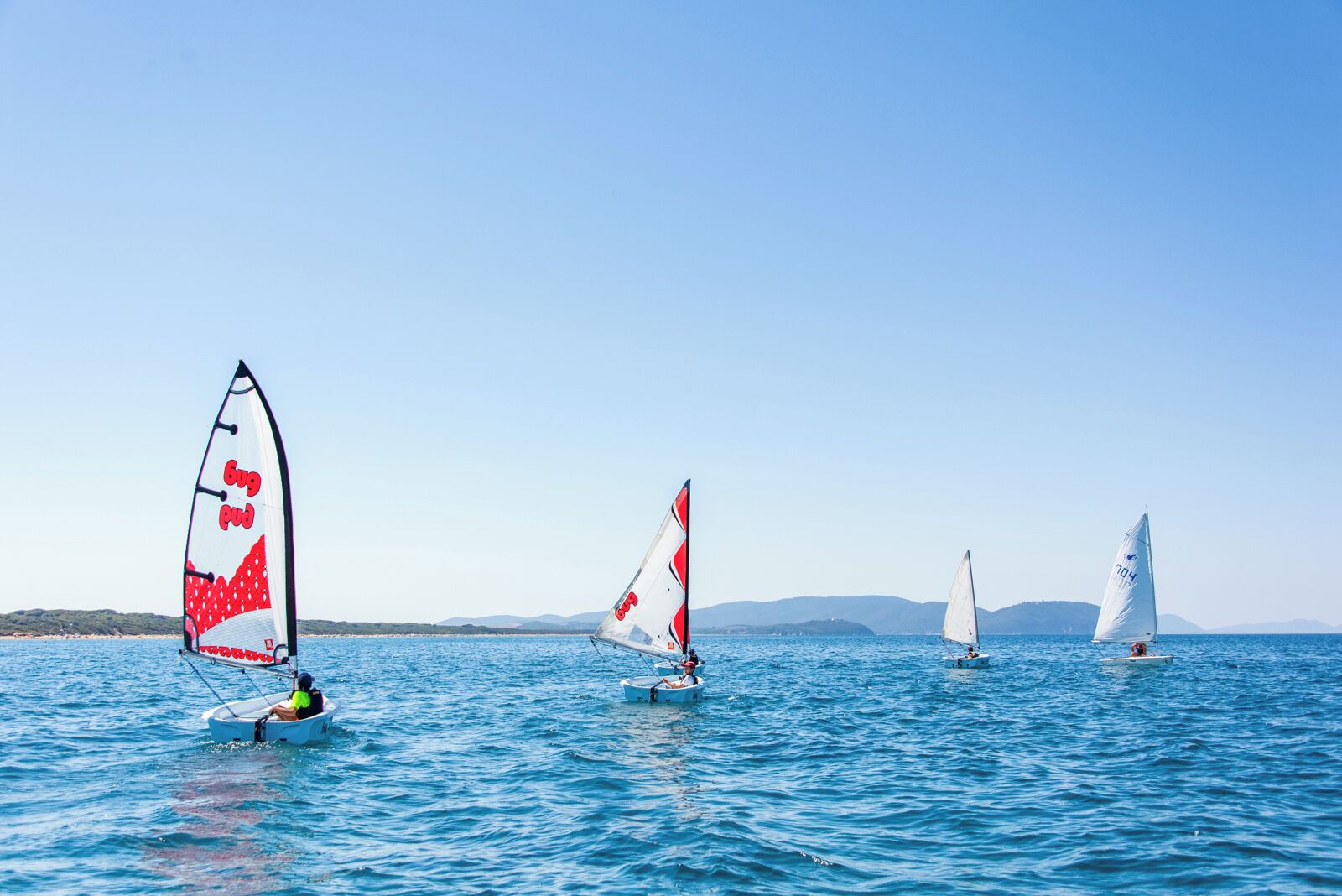 A sailboat with a red and white sail on a calm sea.