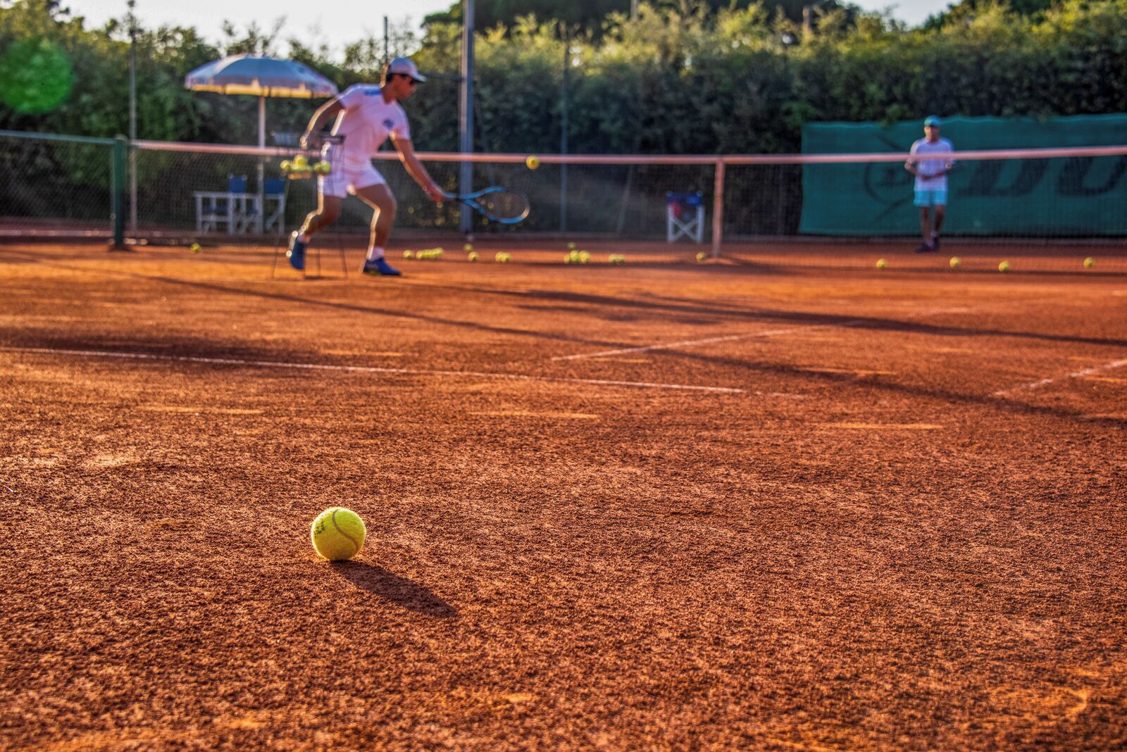 A tennis court with a net, a tennis ball, and two players in motion.