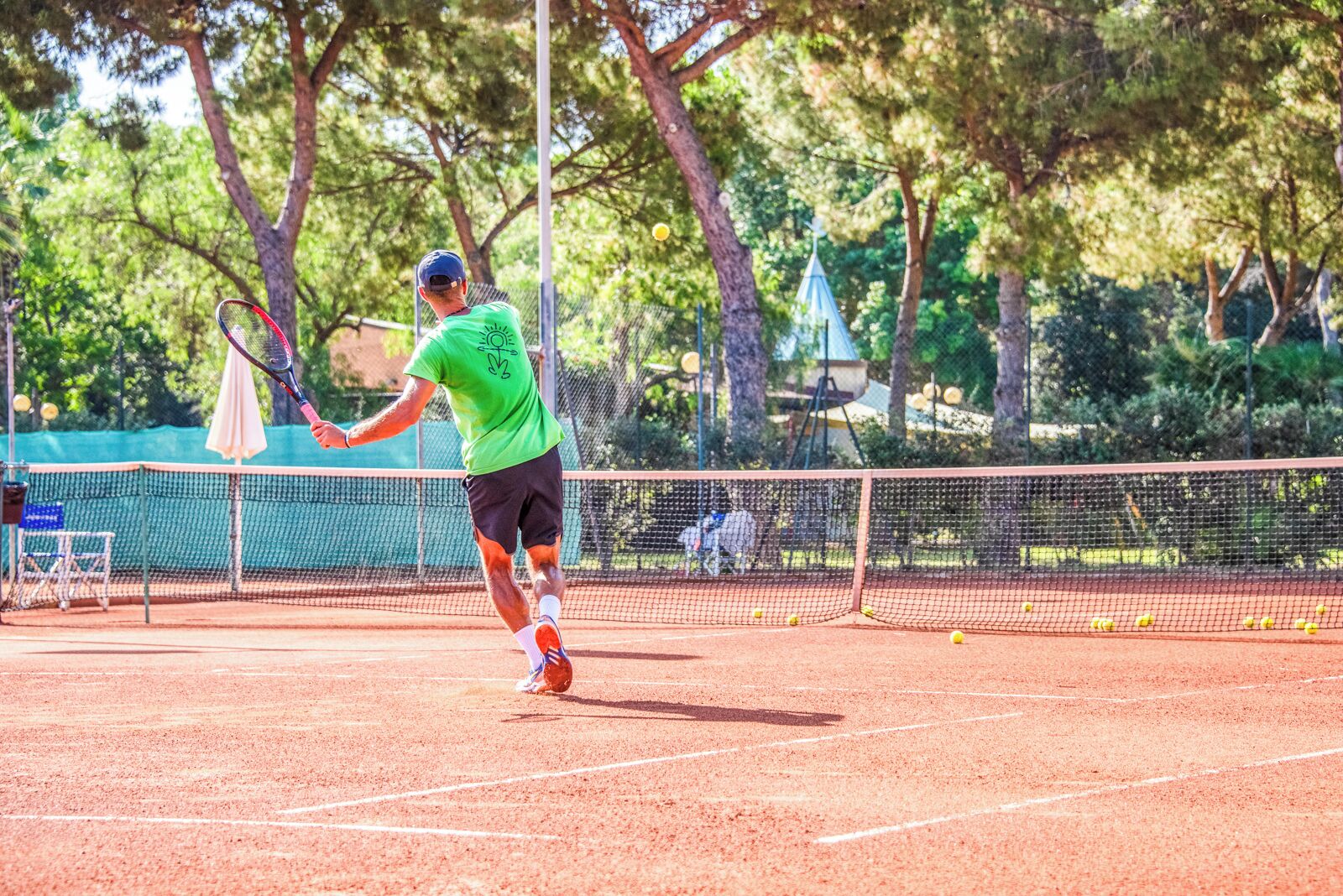 Una cancha de tenis con una red, árboles y una tienda de campaña al fondo.